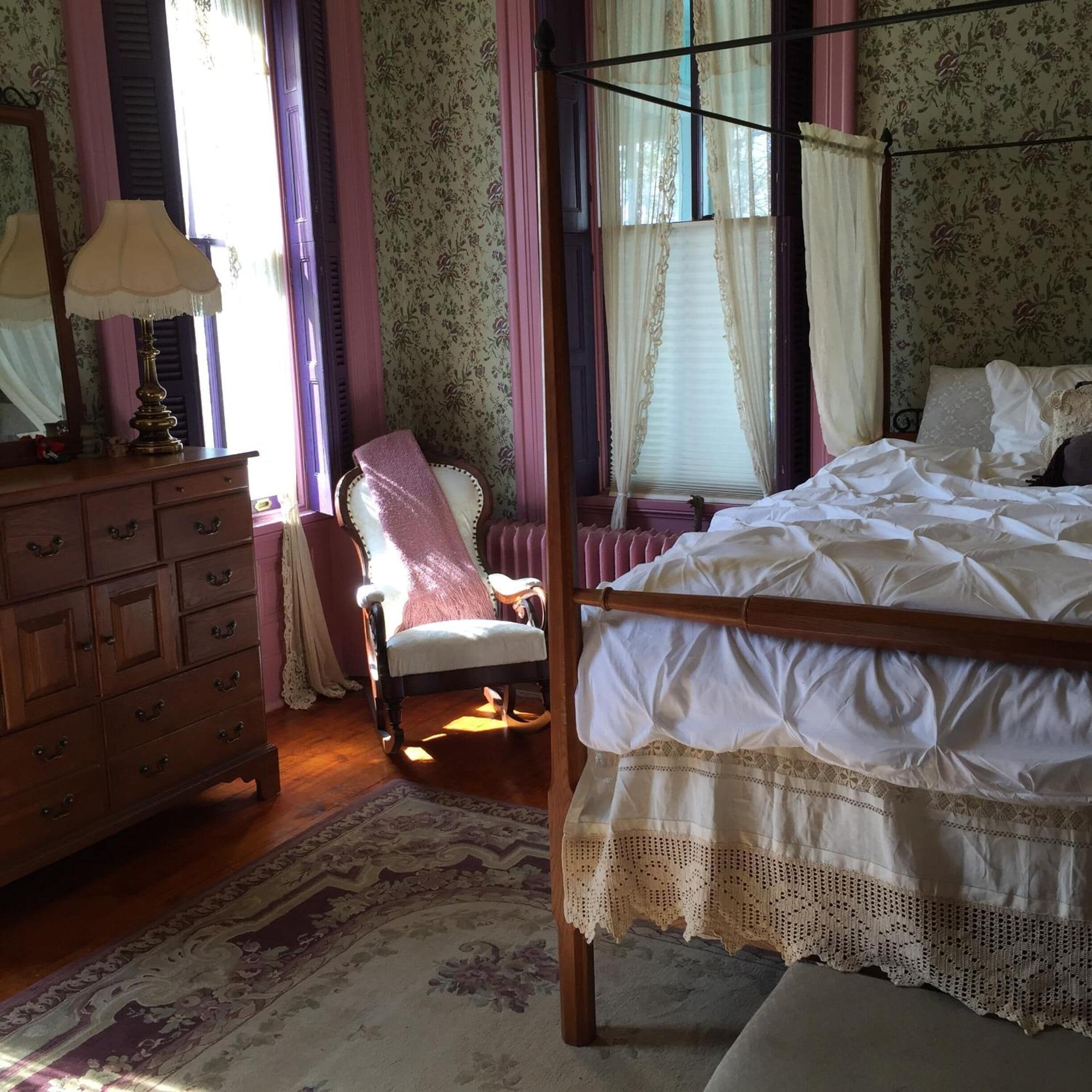 A bedroom with a wooden bed, a wooden dresser, a chair, and a window with curtains.