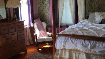 A bedroom with a wooden bed, a wooden dresser, a chair, and a window with curtains.