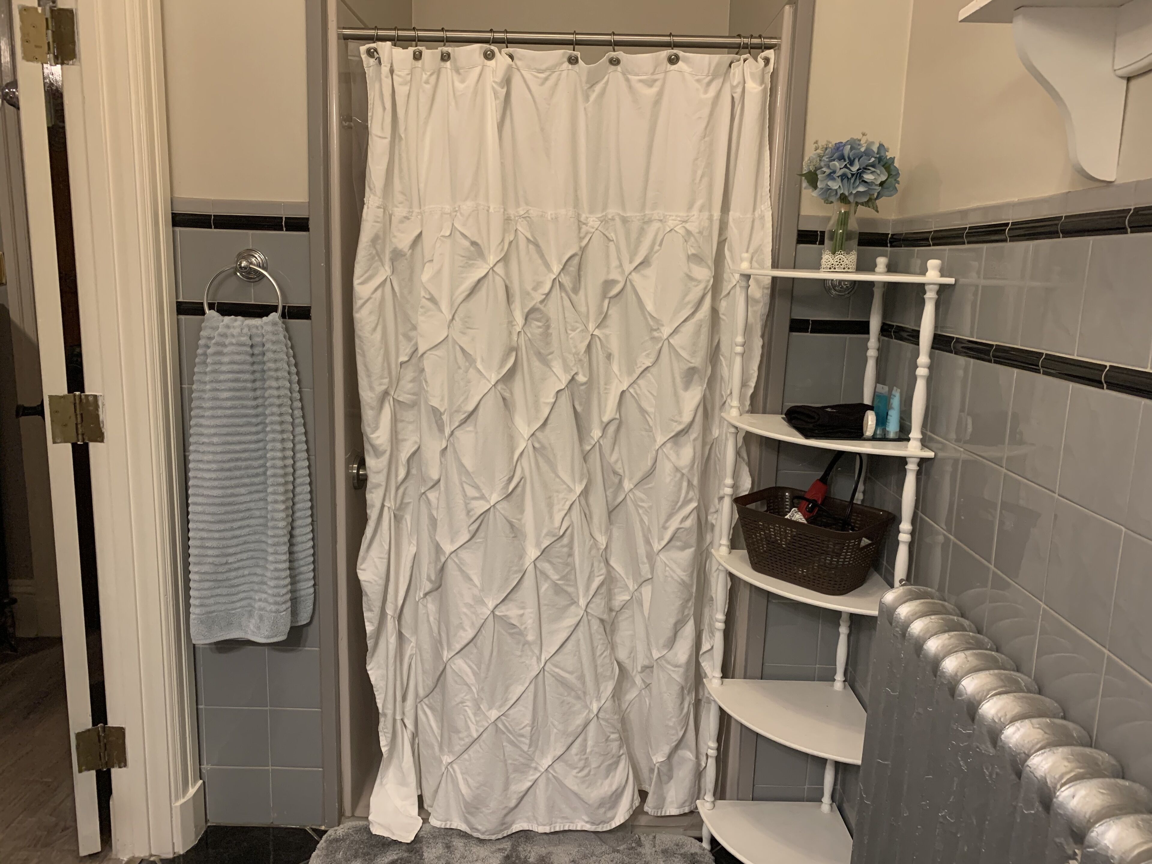 A bathroom with a white shower curtain, a towel rack with a towel, a shelf with toiletries, and a basket.