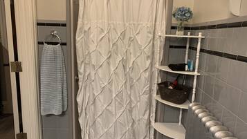 A bathroom with a white shower curtain, a towel rack with a towel, a shelf with toiletries, and a basket.