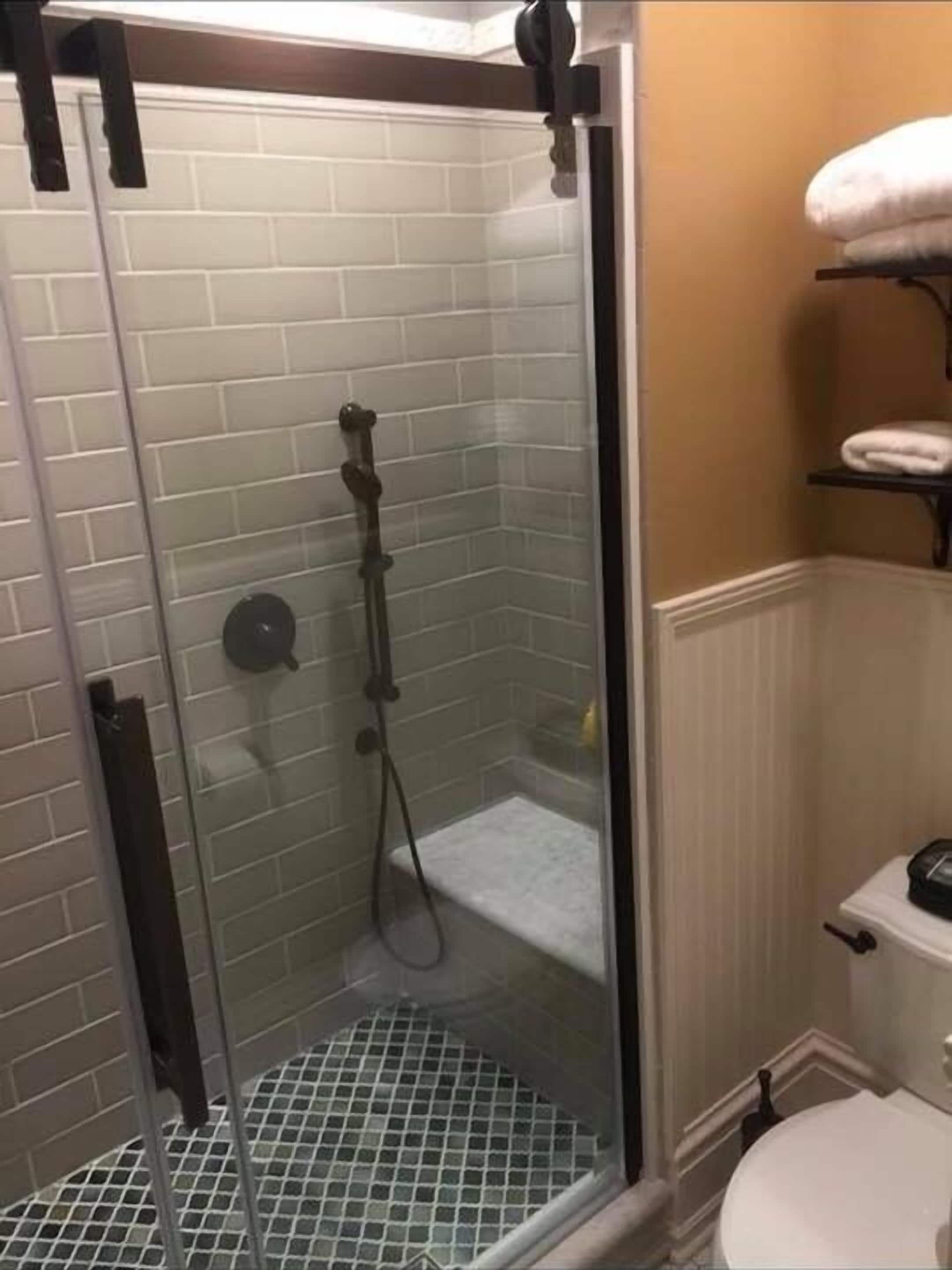 A shower with a glass door, a tiled wall, and a white toilet with a towel rack above it.