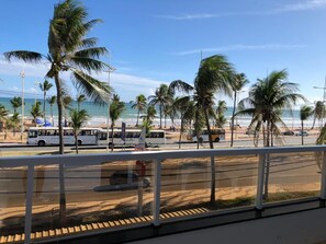 A beachside view with palm trees, a road, and a bus. - Hotel Lazer Piatã (Salvador)