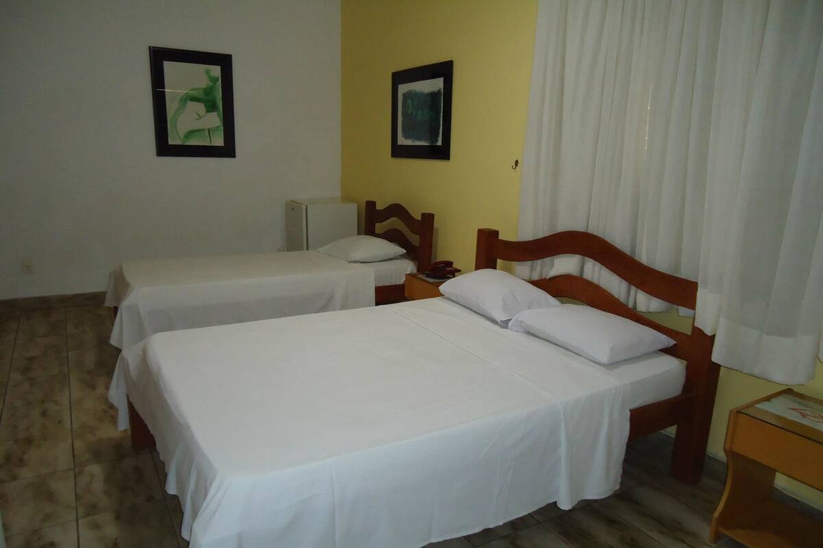 Une chambre d’hôtel avec deux lits simples, une tête de lit en bois, une petite table de chevet et une commode.