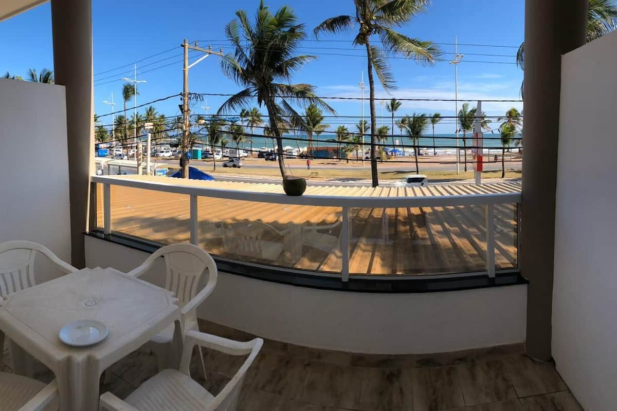 Un balcon avec vue sur la plage, les palmiers et un ciel dégagé.