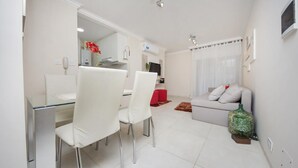 A modern living room with a glass dining table, white chairs, a grey sofa, and a red ottoman. - San Juan Flat 33W (Rio Cuarto)