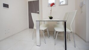 A modern dining area with a glass table, four white chairs, a potted red flower, and two framed mirrors on the wall. - San Juan Flat 33W (Rio Cuarto)