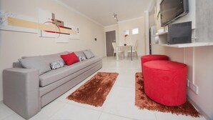 A modern living room with a grey sofa, red ottoman, and a brown rug. - San Juan Flat 33W (Rio Cuarto)
