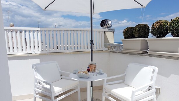 Un área de estar exterior blanca con dos sillas, una mesa, una cerca blanca y plantas en macetas al fondo.