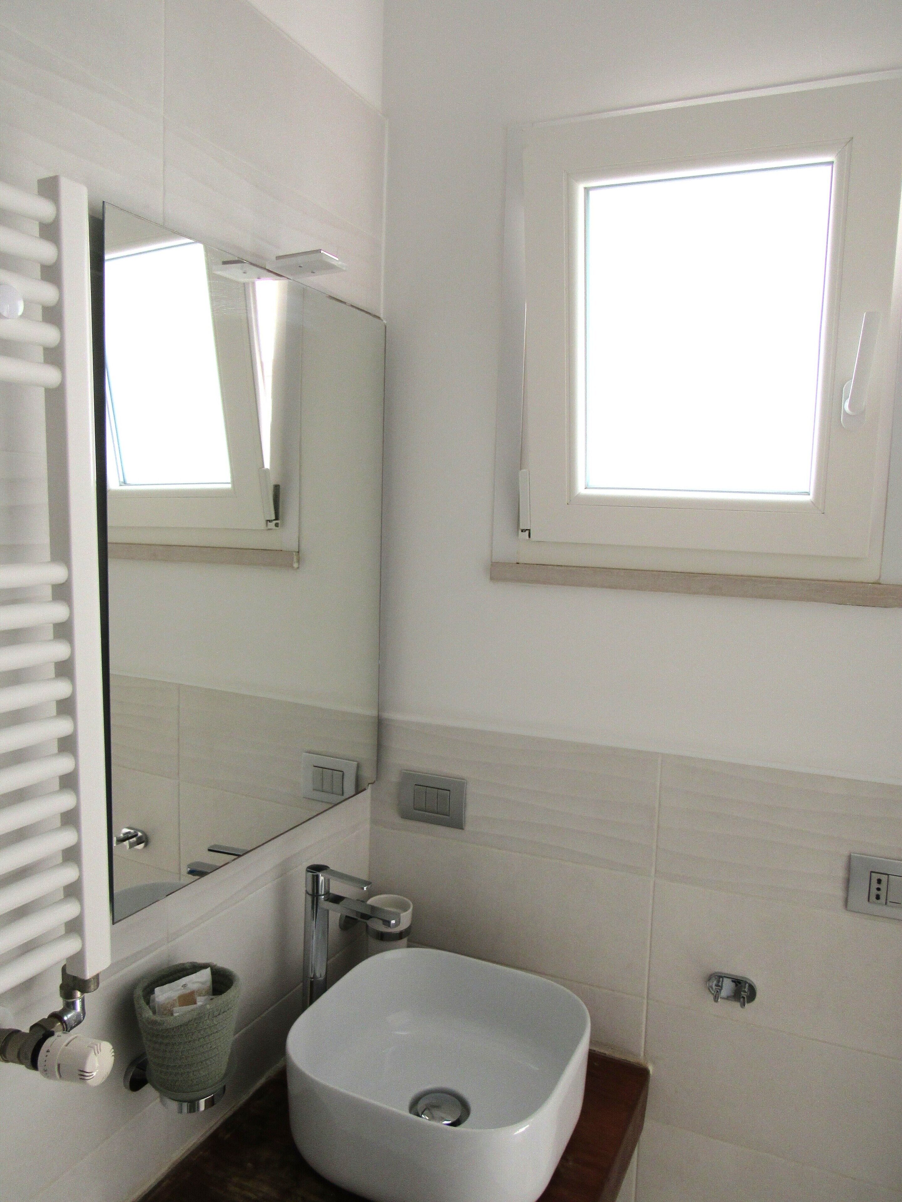 A bathroom with a white sink, a mirror, a window, and a towel rack.