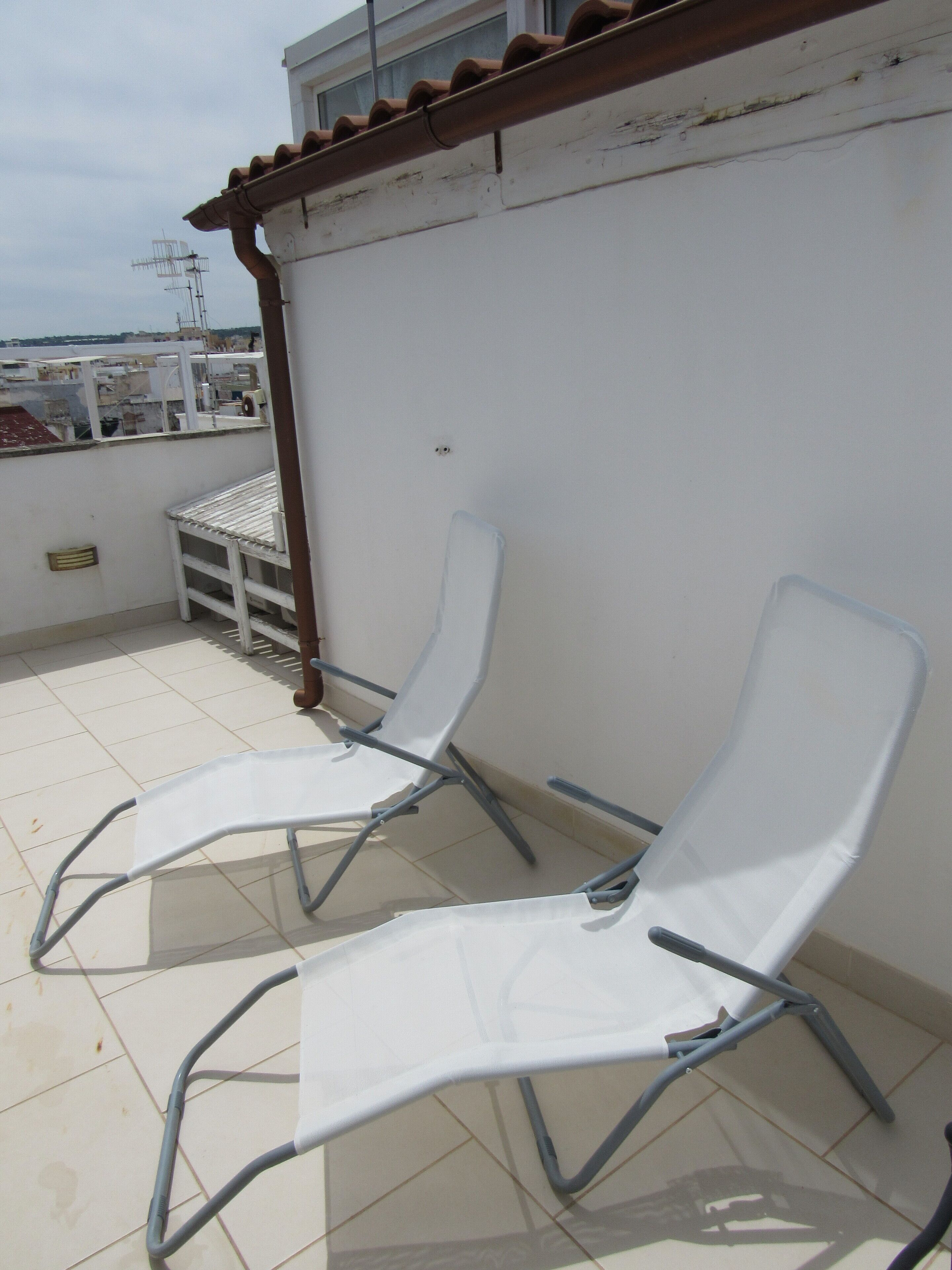 Une terrasse sur le toit avec deux chaises longues blanches, une petite table et une structure en forme de pergola.