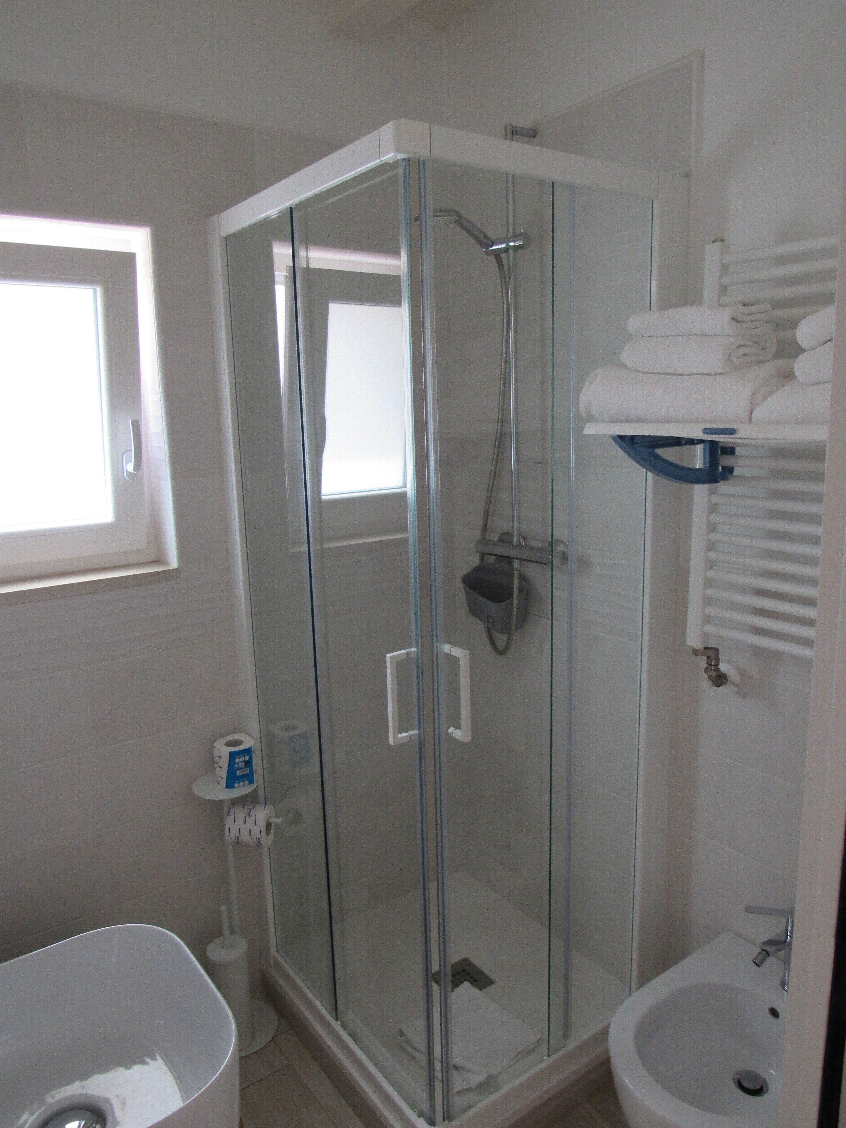 Een moderne badkamer met een douchecabine van glas, een witte badkuip en een klein wastafeltje.