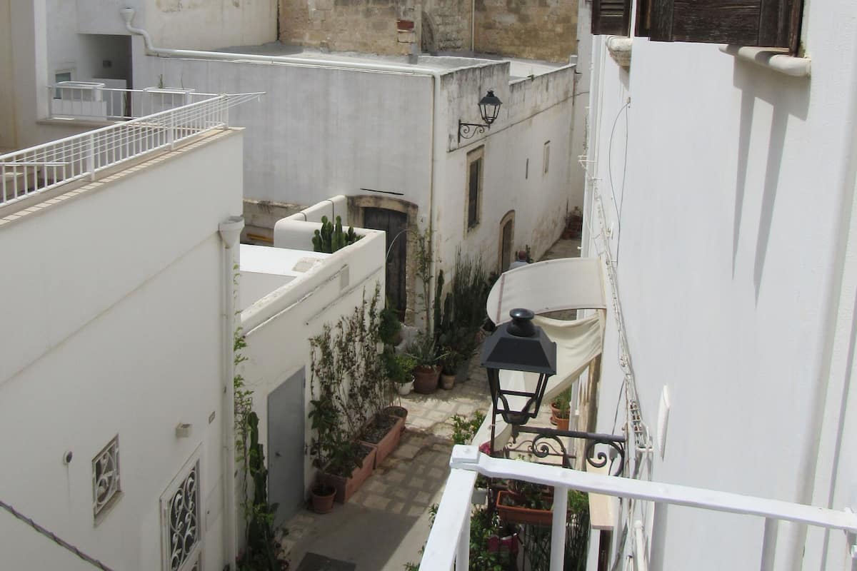 A narrow alleyway with buildings on either side, a small courtyard with potted plants, and a distant church tower.