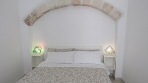 Un dormitorio con una cama bajo un arco de piedra, dos mesitas de noche con lámparas y un edredón estampado.