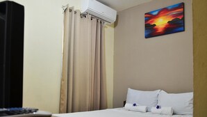 A hotel room with a bed, a painting of a sunset, an air conditioner, and a curtain. - Cabinas Coco Alegre (Sardinal)