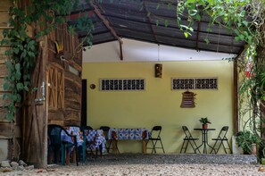 A rustic wooden door with a metal gate, a covered patio area with a table and chairs, and a wall with two barred windows. - Cabinas Coco Alegre (Sardinal)