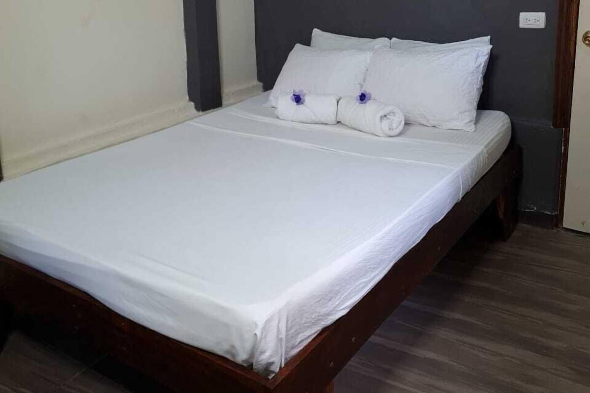 A single bed with white linens, a wooden headboard, and a dark gray wall.