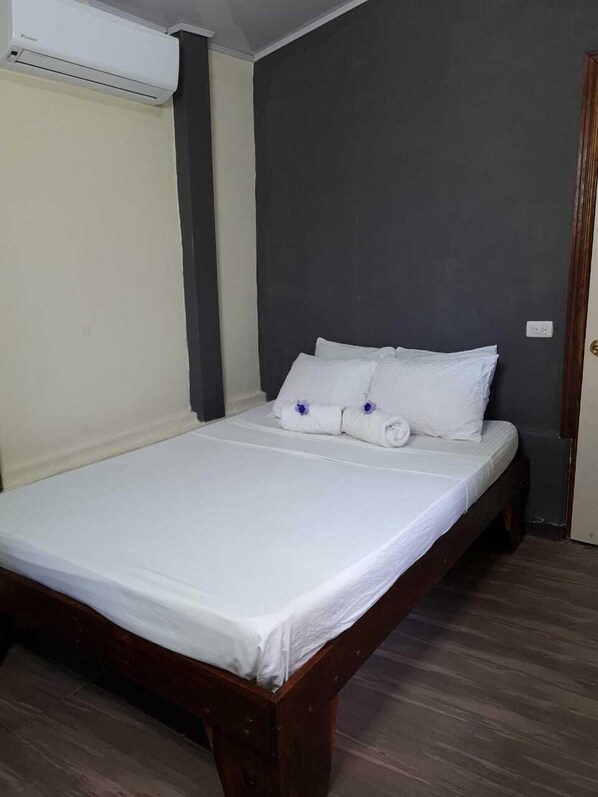 A single bed with white linens, a wooden headboard, and a dark gray wall. - Cabinas Coco Alegre (Sardinal)
