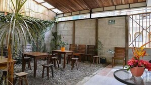 An indoor patio area with wooden tables and chairs, surrounded by potted plants and a gravel floor. - Cabinas Coco Alegre (Sardinal)