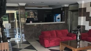 Un hall d’hôtel avec un comptoir d’enregistrement, un canapé rouge, une table basse et un sol carrelé.