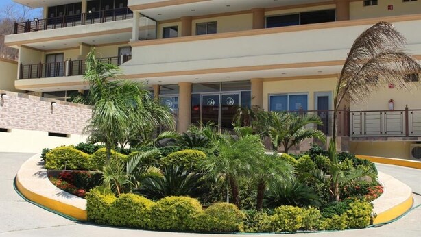 Un hôtel à plusieurs étages doté d’un jardin aménagé avec des palmiers et des arbustes.