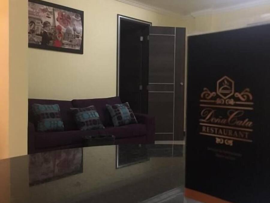 Un área de recepción con un mostrador oscuro, un sofá morado con cojines estampados, un cuadro en la pared y una puerta que da al restaurante.