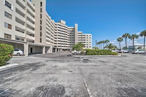 Un hotel de varios pisos con estacionamiento, palmeras y un cielo azul despejado.
