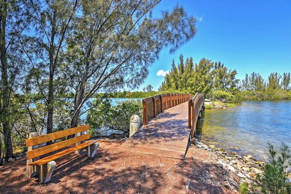 Un puente de madera que conduce a un banco junto a un lago rodeado de árboles.