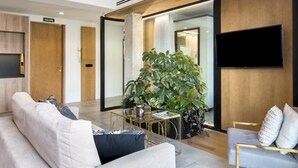 Een moderne hotellobby met een bank, een bijzettafeltje, een grote plant en een tv aan de muur.