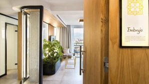 Een modern kantoorinrichting met een houten deur, een kunstwerk in een lijst getiteld 'Embrujo', en een stadsgezicht door grote ramen.