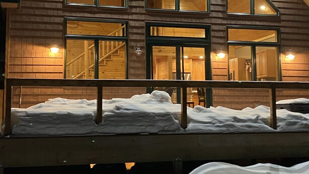 Puinen mökki, jossa on useita suuria ikkunoita, katettu terassi ja portaat, jotka johtavat sisäänkäynnille.