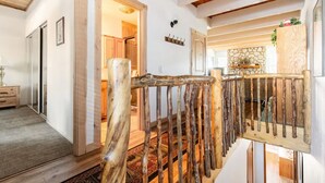 Una escalera de madera de diseño rústico que conduce a una habitación con chimenea de piedra y techo de madera.