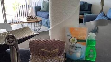 A kitchen counter with a paper towel roll, a woven cloth, a dishwashing liquid bottle, and a sponge.