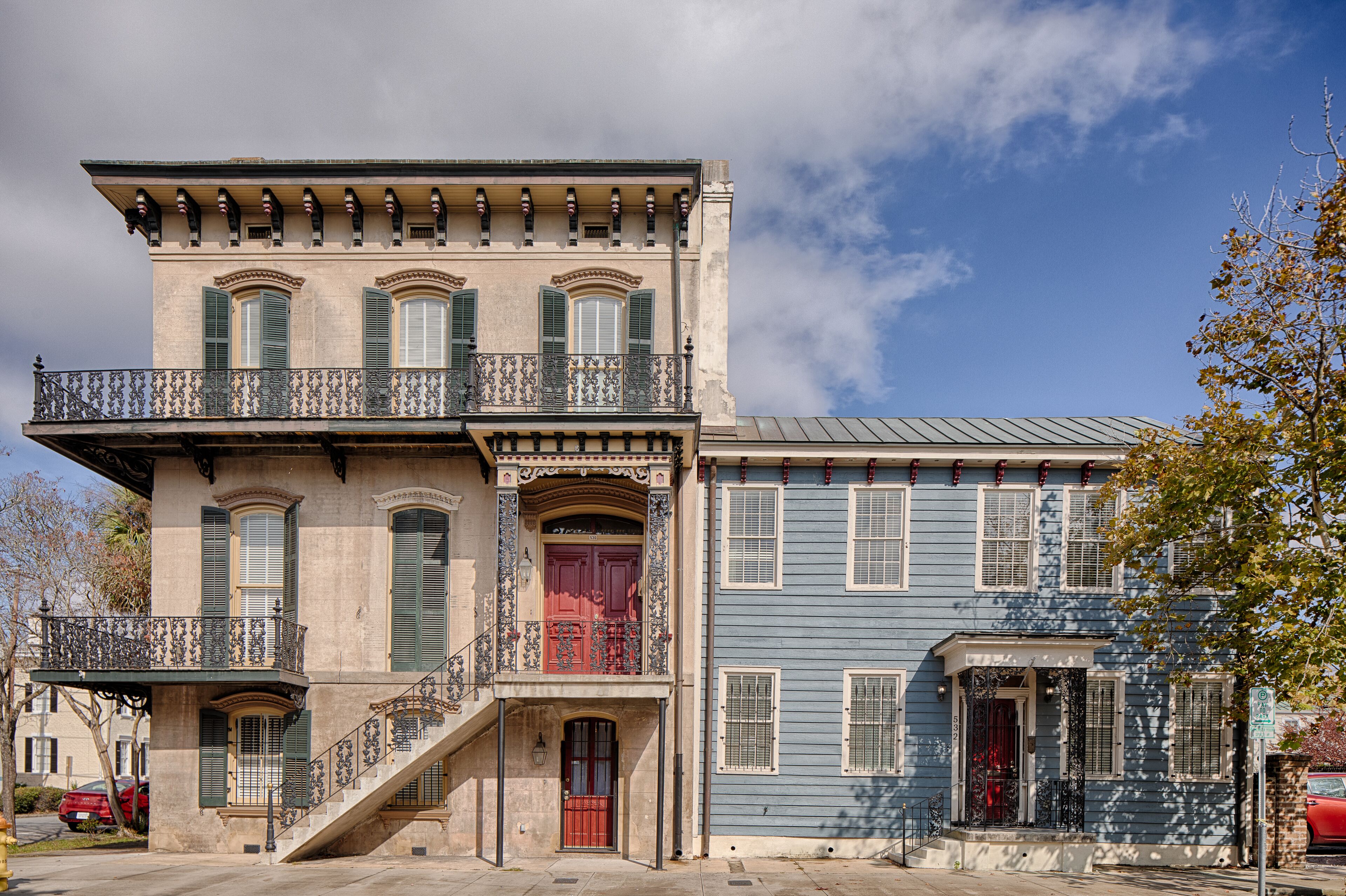 A two-story building with a balcony, a red door, and a staircase leading to the entrance.