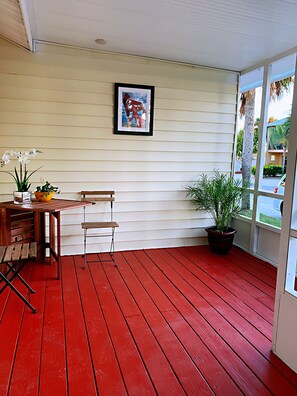 Ein Zimmer mit rotem Holzboden, einem Holztisch mit Stühlen, einem Blumentopf und einem gerahmten Bild an der Wand.