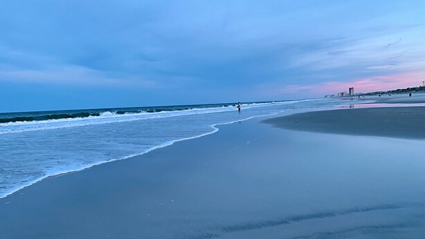 A beach with a wide sandy shore, gentle waves, and a clear sky.