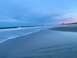 Ein Strand mit breitem Sandufer, sanften Wellen und blauem Himmel.