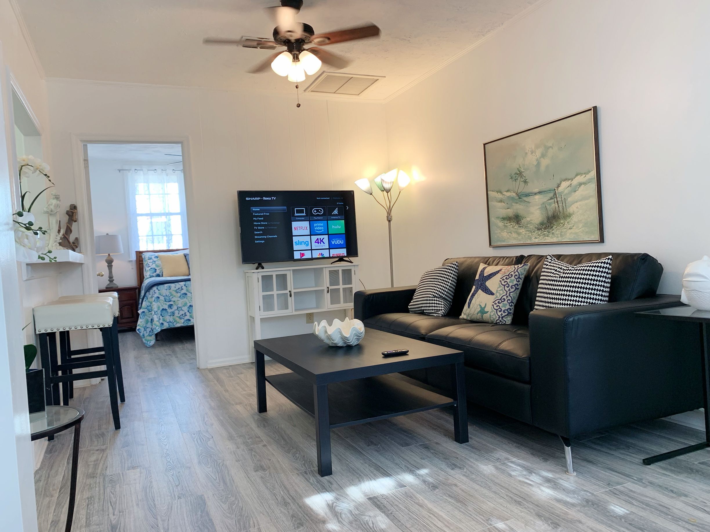 A modern living room with a black sofa, a coffee table, a flat-screen TV, and a ceiling fan.