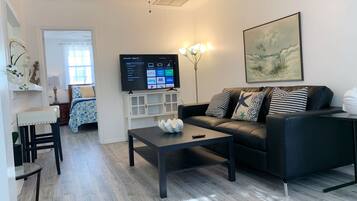 A modern living room with a black sofa, a coffee table, a flat-screen TV, and a ceiling fan.