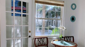 A room with a large window, two wicker chairs, a small table, and decorative wall mirrors.