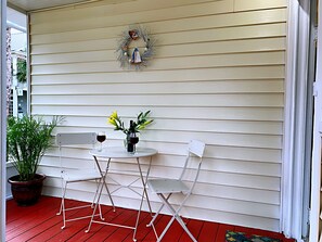 A small outdoor seating area with a table and two chairs, a potted plant, and a decorative wreath on the wall.