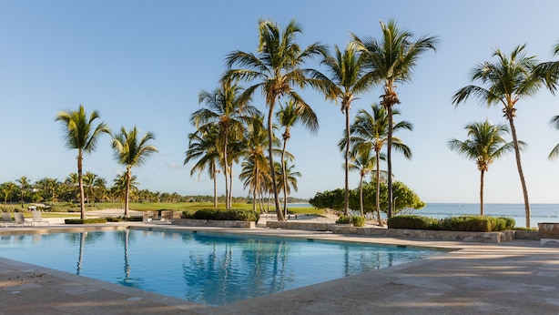 Ein Poolbereich mit Palmen und Blick aufs Meer.