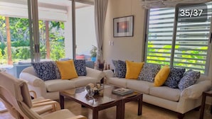 Ein Wohnzimmer mit zwei Sofas, einem Couchtisch und einem Sessel. Ein Fenster mit Jalousien und ein Bild an der Wand.