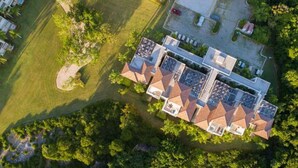 Eine Vogelperspektive zeigt ein modernes Hotel mit mehreren Gebäuden, die durch Laubengänge verbunden sind, umgeben von üppiger Vegetation und einem gepflegten Rasen.