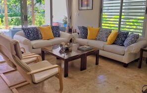 A living room with two sofas, a coffee table, and a chair. There is a window with blinds and a picture on the wall.
