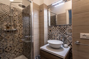 A modern bathroom with patterned tiles, a glass shower enclosure, a white sink, and a mirror. - "Moon river" Comfort House in Verona (Verona)