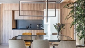 Un comedor moderno con una mesa de vidrio rodeada de sillas, paneles de madera en las paredes y una planta grande a la derecha.