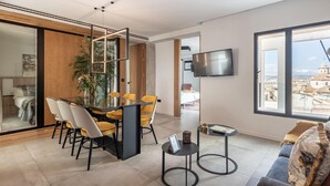 Una sala de estar moderna con comedor, televisor montado en la pared y un amplio ventanal con vistas a la ciudad.