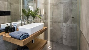 Un baño moderno con un lavabo rectangular, cabina de ducha de vidrio y tocador de madera.