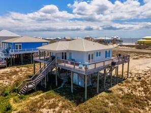Una casa frente a la playa con una terraza de madera y una escalera que conduce a la entrada principal.