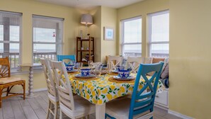A dining area with a table set for six, surrounded by chairs, a lamp, and a bookshelf.